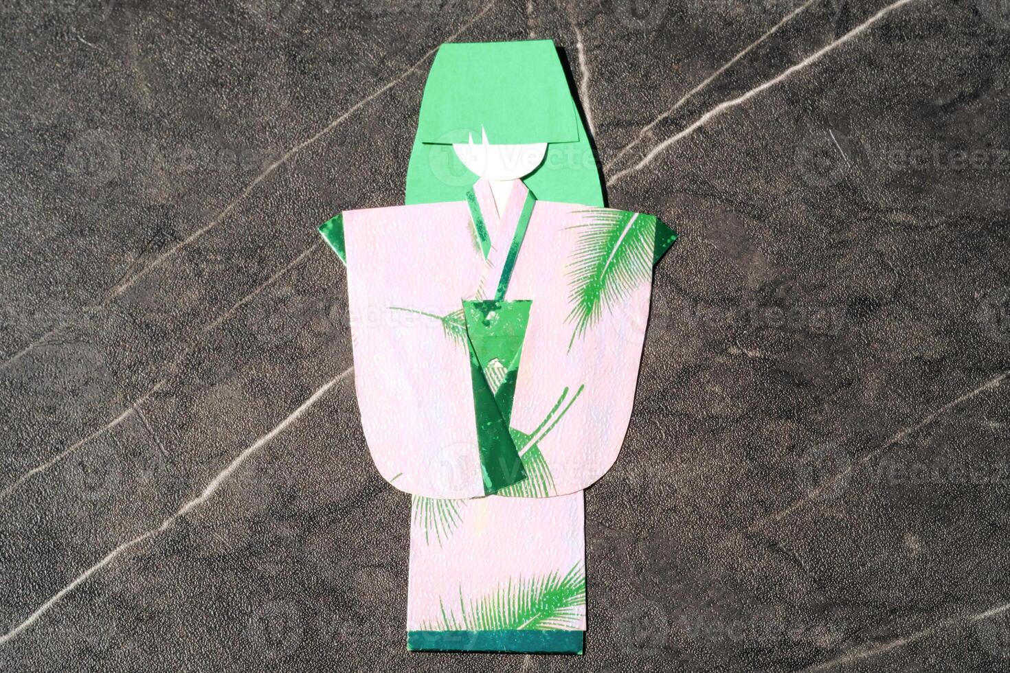 Origami paper in the shape of a woman in a kimono. Green paper is used for hair and pink paper is used for kimono clothes. The art of paper folding. Origami craft isolated in black photo