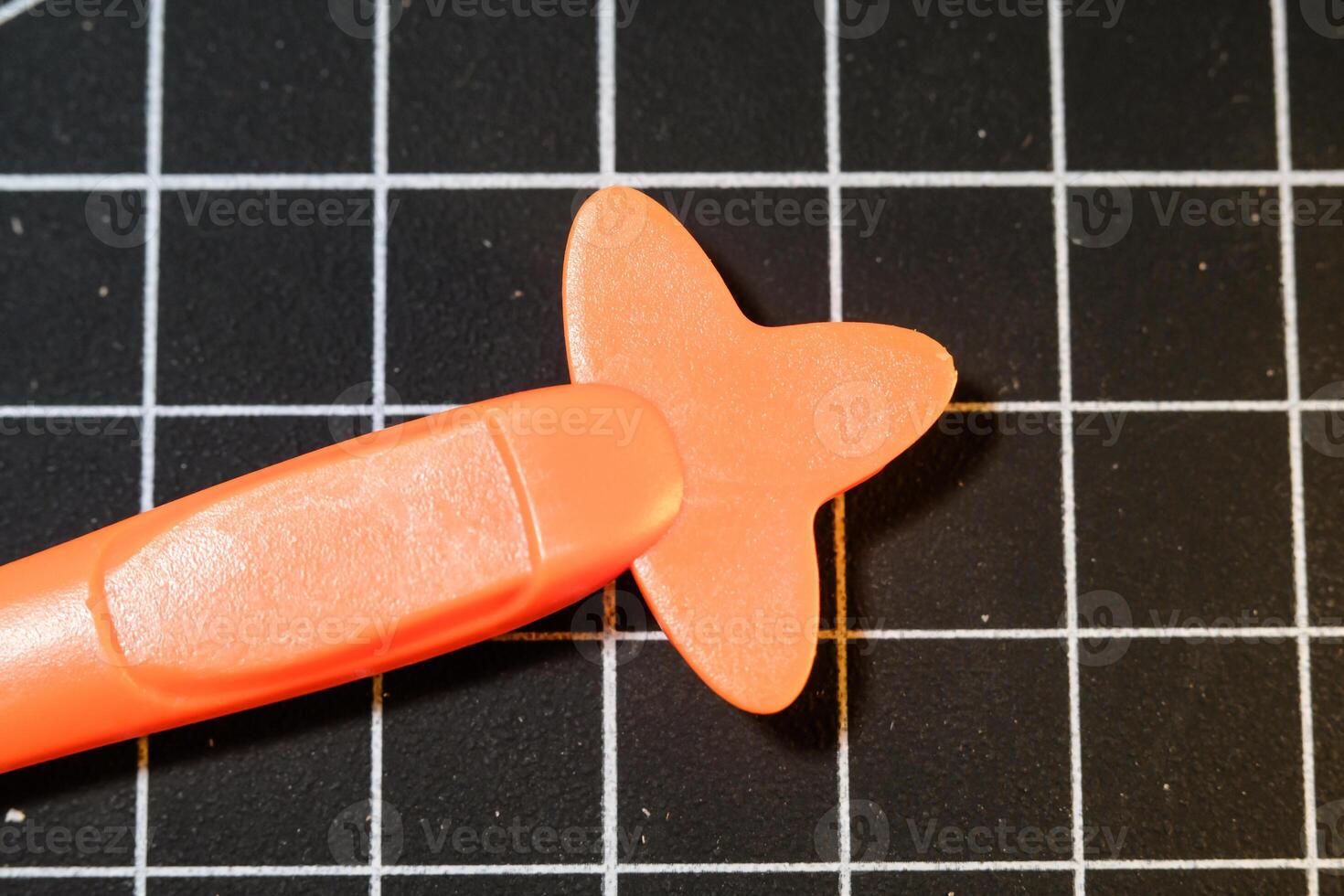 Closeup Orange Plastic opener on black striped rubber mat. Plastic opener is used to remove and disassemble model kits parts that have been installed. Plastic tools and equipment for hobbyists. photo