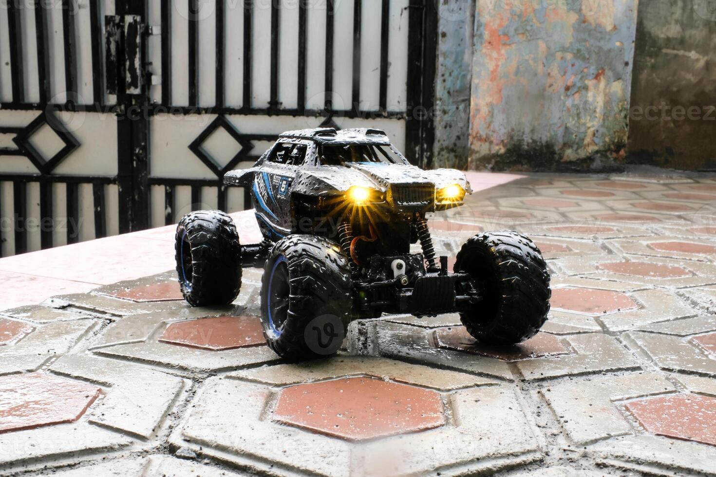 Toy car during outdoor rain with lights on. Remote Control Car being played in the yard during rain. Hobbies and Leisures. Graphic Resources. Toy Photography Concepts photo