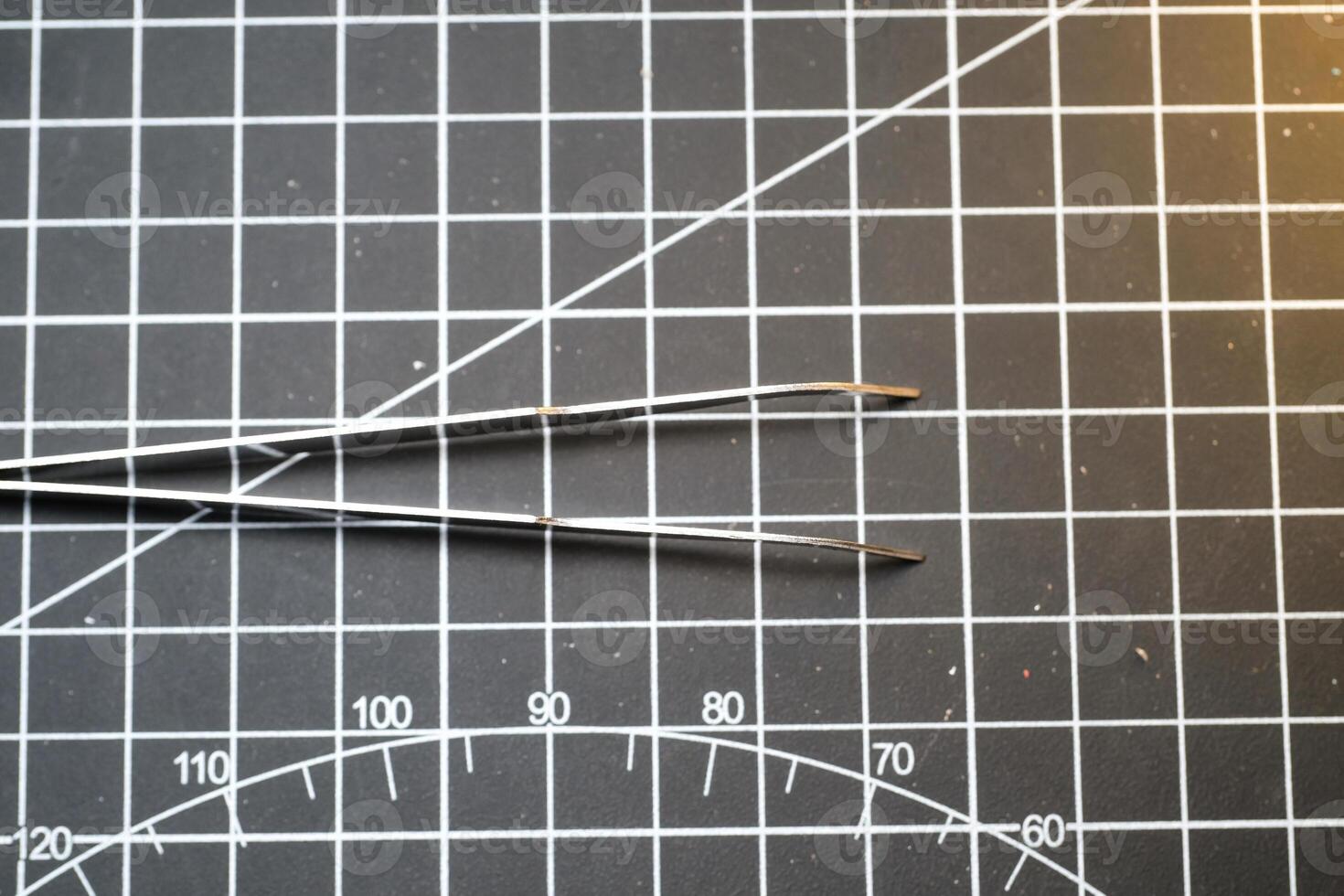 Closeup of metal precision tweezer with pointed tip. Tweezer is on a black cutting mat with lines. A tool that functions to clamp and pull out small objects. Negative Space photo