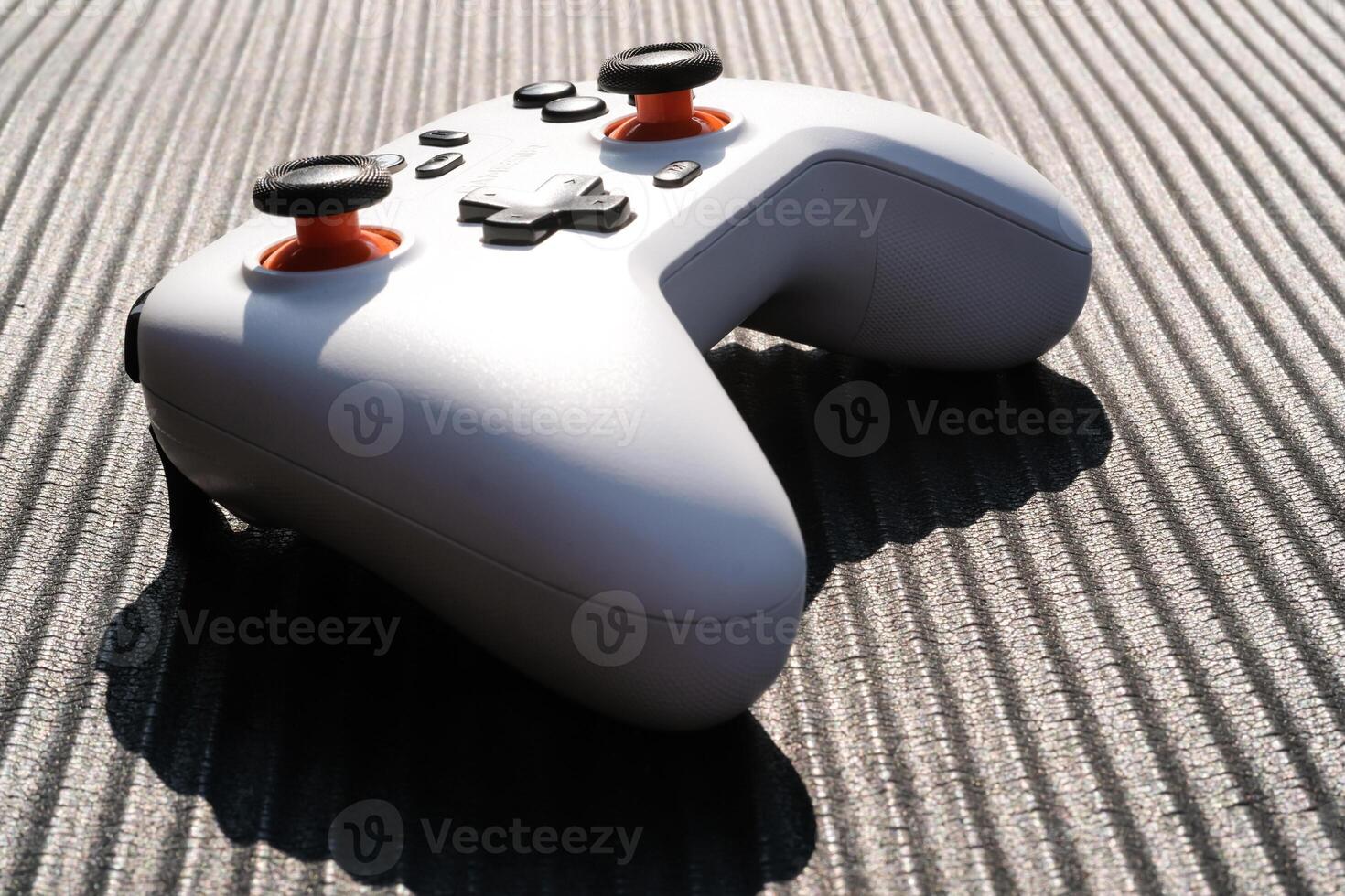 A Gamepad with a black striped background. The wireless gamepad has a dominant white color with orange on the joystick and black on each button. Game Controller isolated. Negative space photo