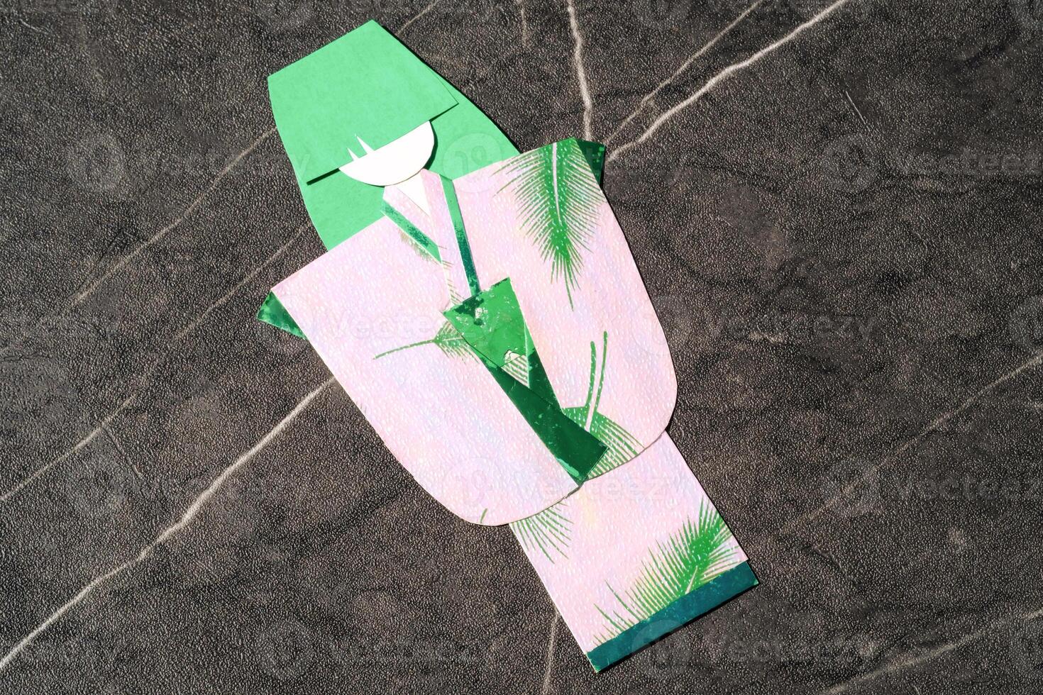 Origami paper in the shape of a woman in a kimono. Green paper is used for hair and pink paper is used for kimono clothes. The art of paper folding. Origami craft isolated in black background photo