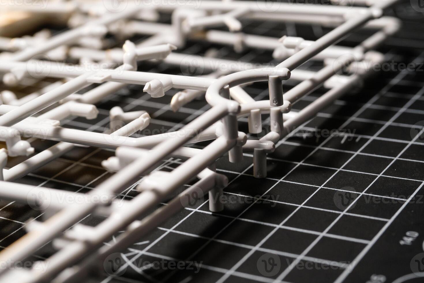 Stack of white Plastic Frames on Black rubber cutting mat. Abstract Backgrounds of model kit frames. Part of plastic model kit and tools for building robot. Miniature, Frame, Plastic photo