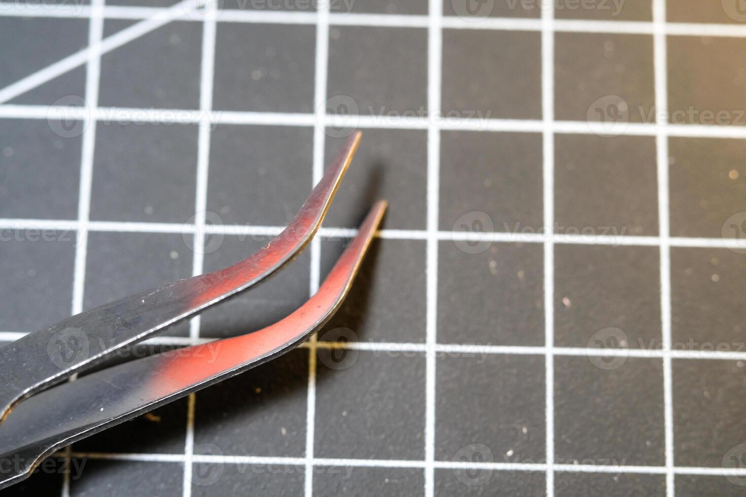 Metal precision tweezer with pointed tip. Tweezer is on a black cutting mat with lines. A tool that functions to clamp and pull out small objects. Negative Space photo