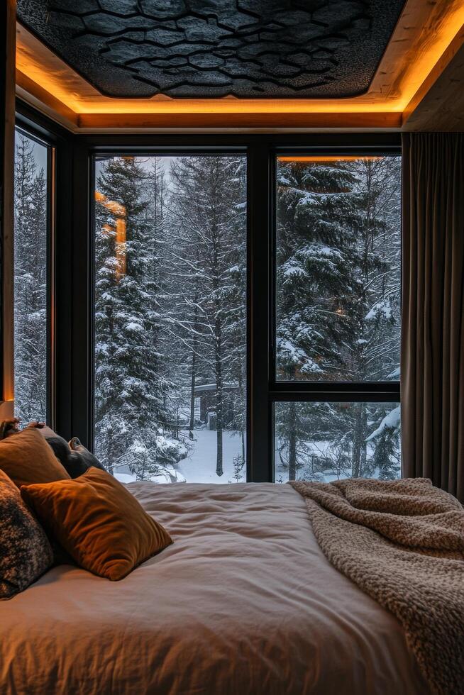 A bedroom with a bed and windows overlooking a snowy forest photo