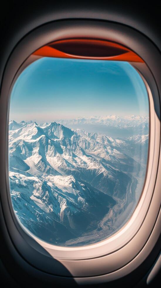 An airplane window looking out at a snowy mountain range photo