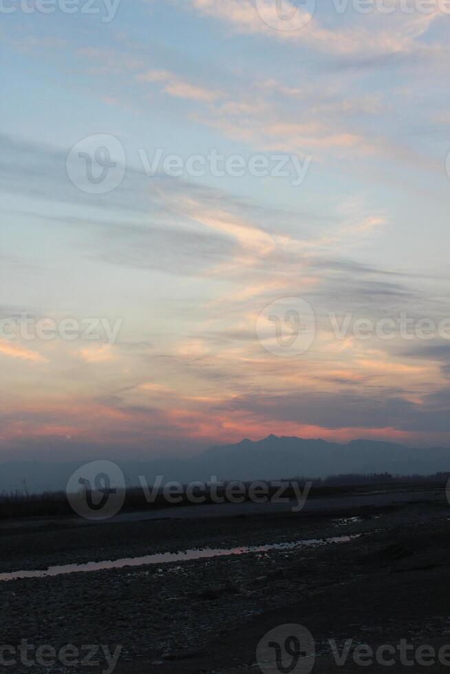 Bare trees are silhouetted against a dusky sky, partially obscured by a setting sun. photo