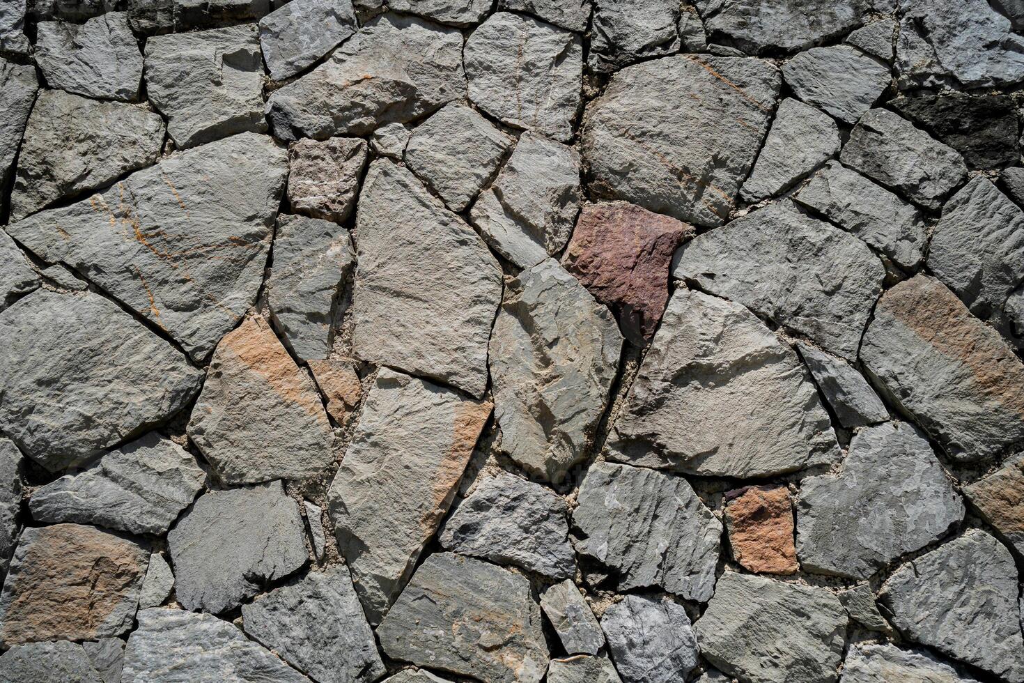 A stone wall with a few large stones and a small one. The wall is made of gray and brown stones photo