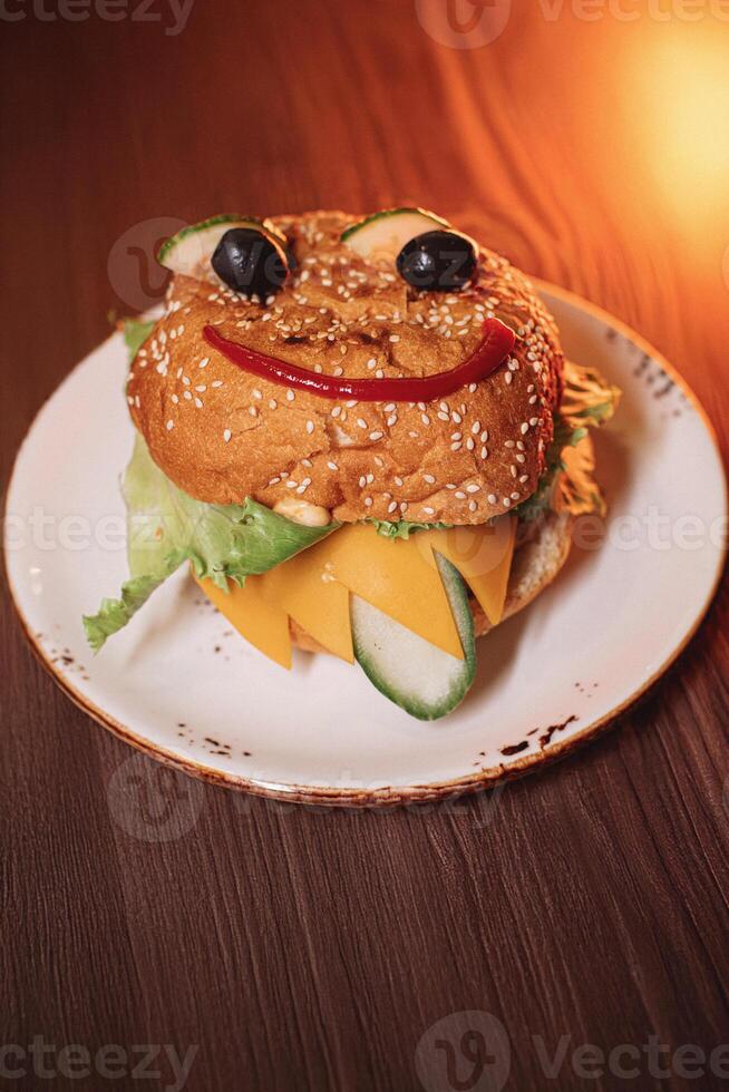juicy children's burger with a painted face made of ketchup, olives and cucumber, burger with chicken cutlet and beef photo