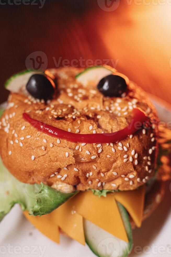 juicy children's burger with a painted face made of ketchup, olives and cucumber, burger with chicken cutlet and beef photo