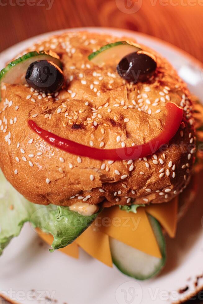 juicy children's burger with a painted face made of ketchup, olives and cucumber, burger with chicken cutlet and beef photo
