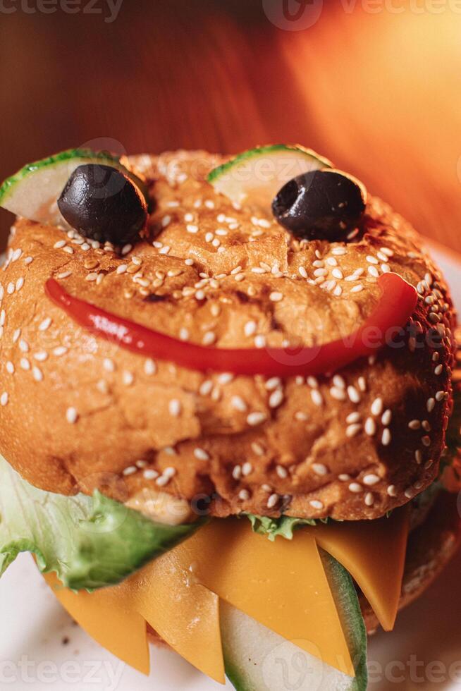 juicy children's burger with a painted face made of ketchup, olives and cucumber, burger with chicken cutlet and beef photo