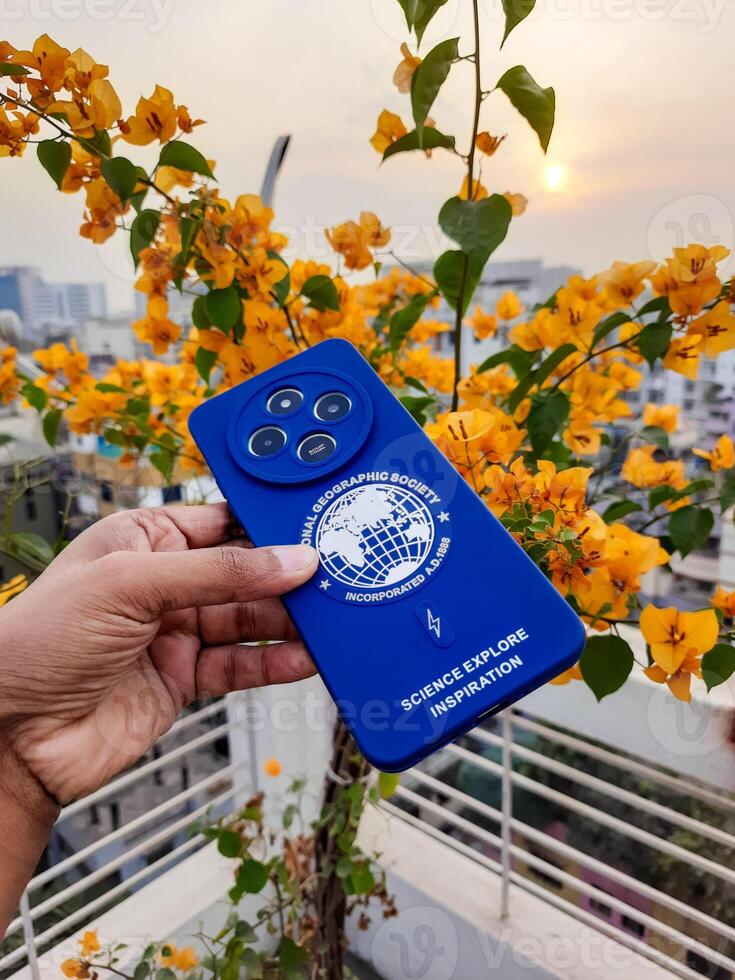 a person holding a blue cell phone with a flower in the background photo