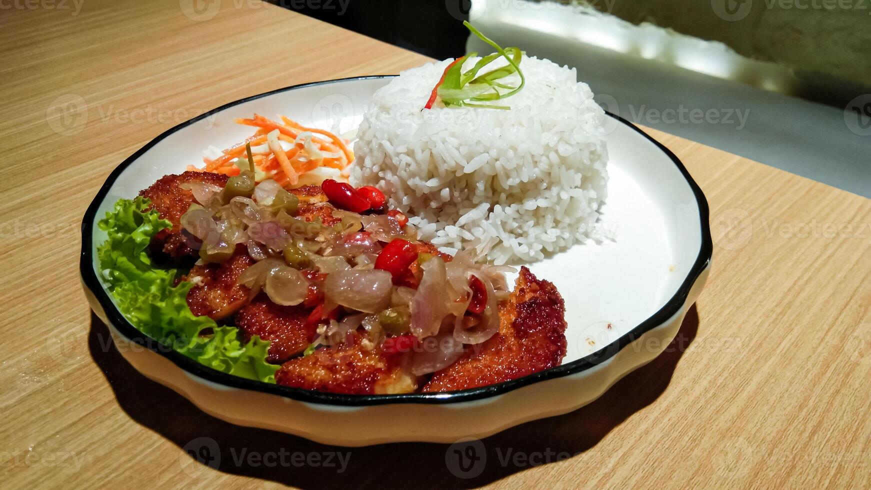 a plate of rice and chicken katsu with sambal matah and fresh vegetables on a wooden table photo
