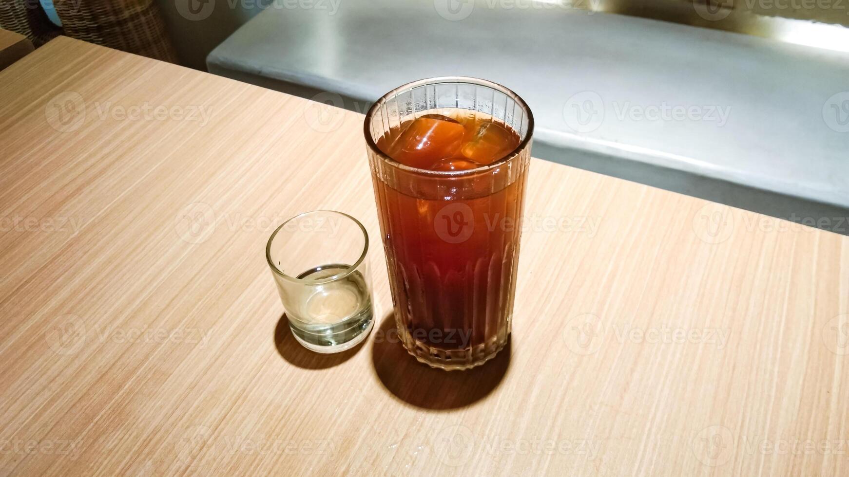 A glass of americano iced with liquid sugar in a small glass, on a wooden table photo