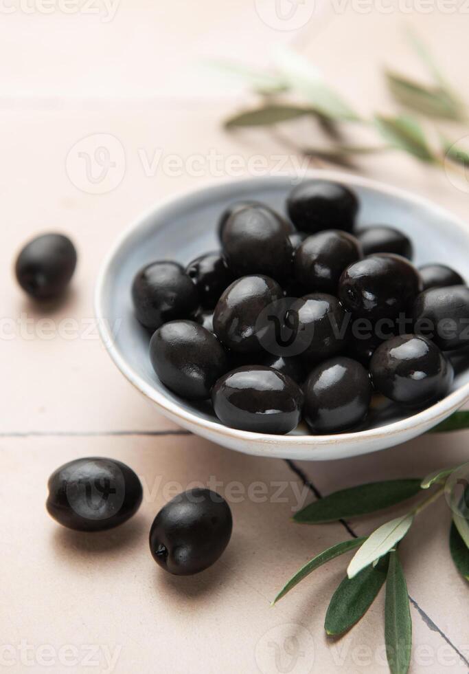 Black olives served in ceramic bowl on hexagonal beige tiles, decorated with olive tree branch photo