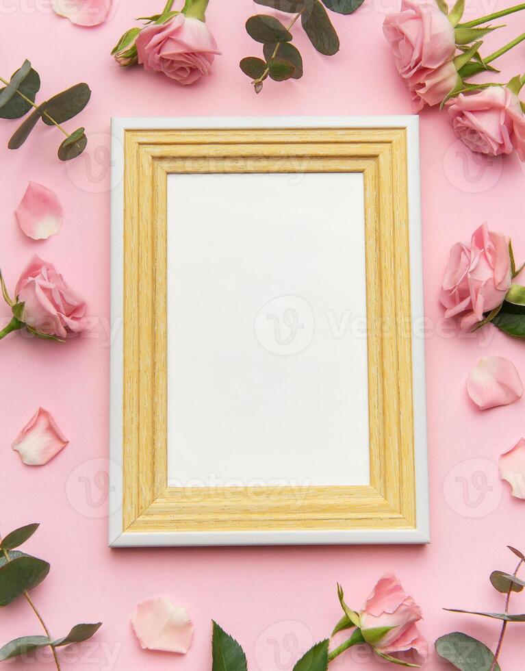 Wooden empty frame decorated with pink roses and eucalyptus leaves on pink background for valentine's day photo