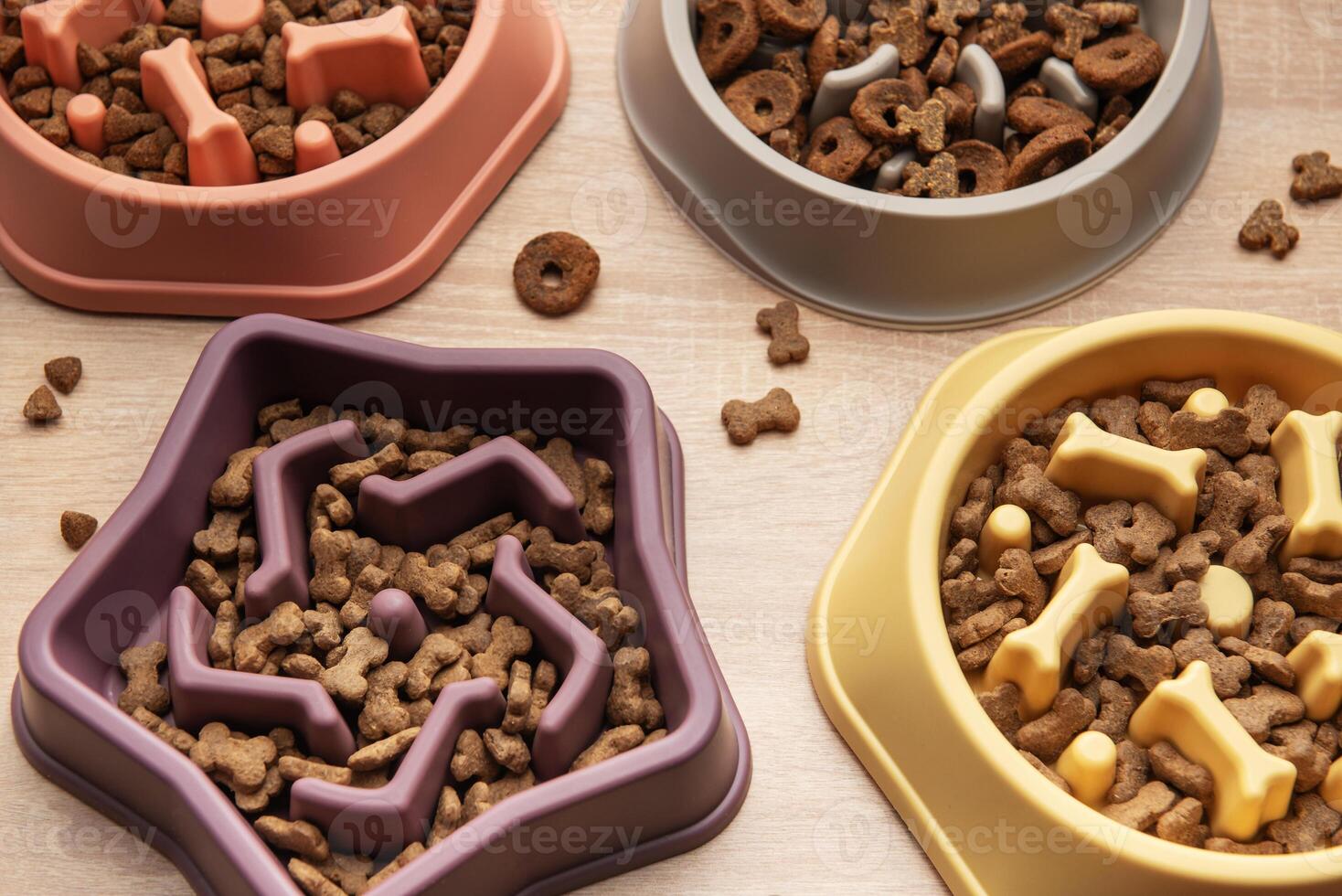 Different shapes of slow feeder bowls with dry food for dogs on wooden surface top view photo