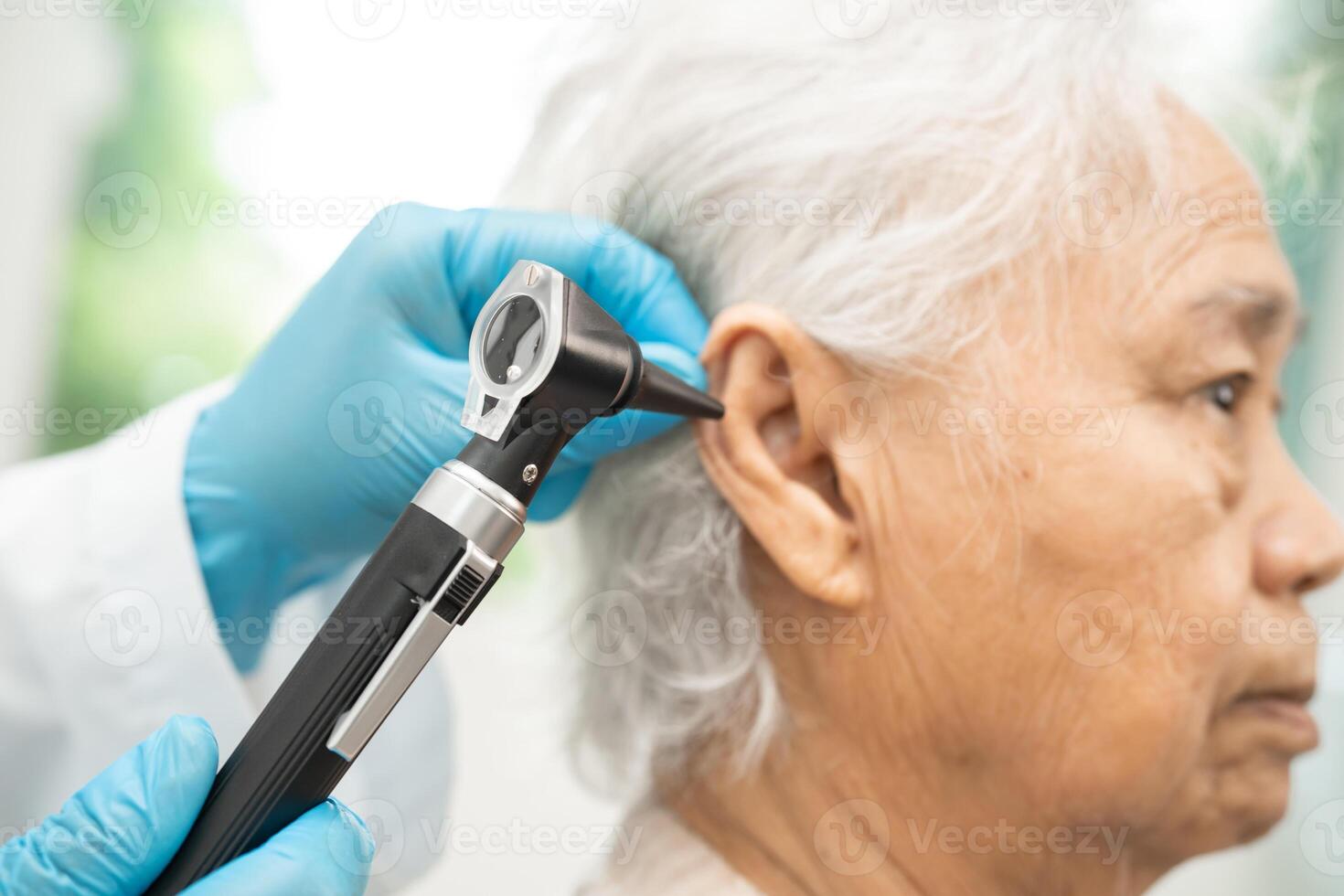Audiologist or ENT doctor use otoscope checking ear of asian senior woman patient photo