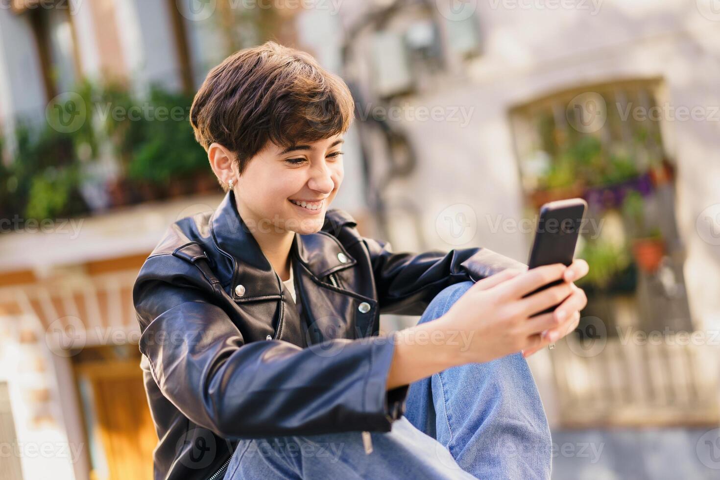 A cheerful young individual is actively engaged with their smartphone in a lively urban setting photo