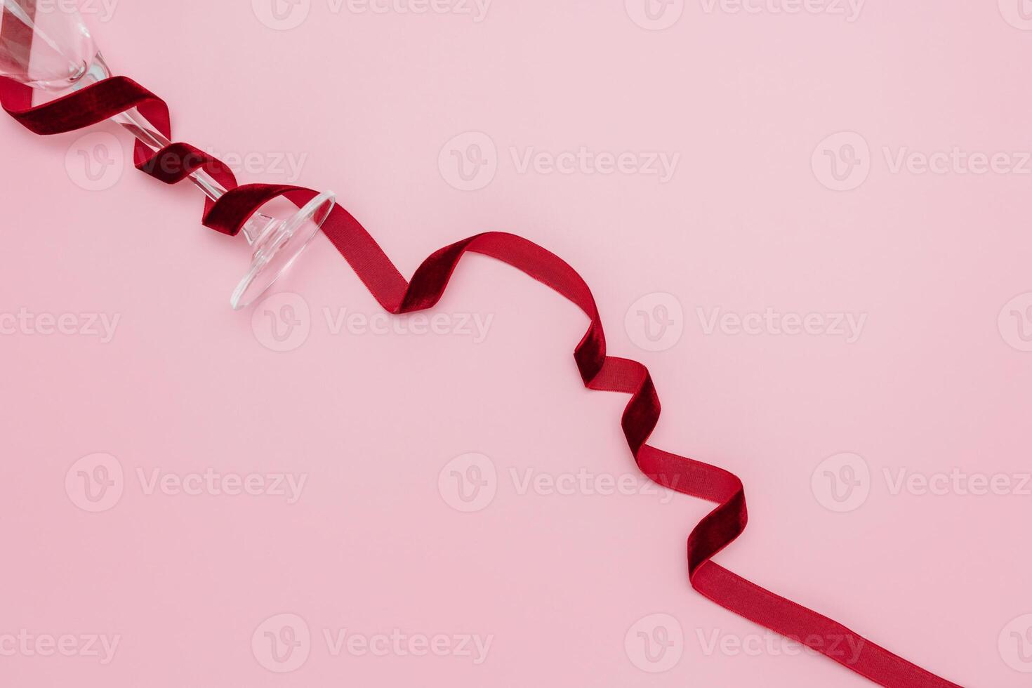 A minimalist and creative composition featuring a wine glass, red velvet ribbon on a soft pink background, representing elegance, Valentines celebration, and sophisticated design. photo