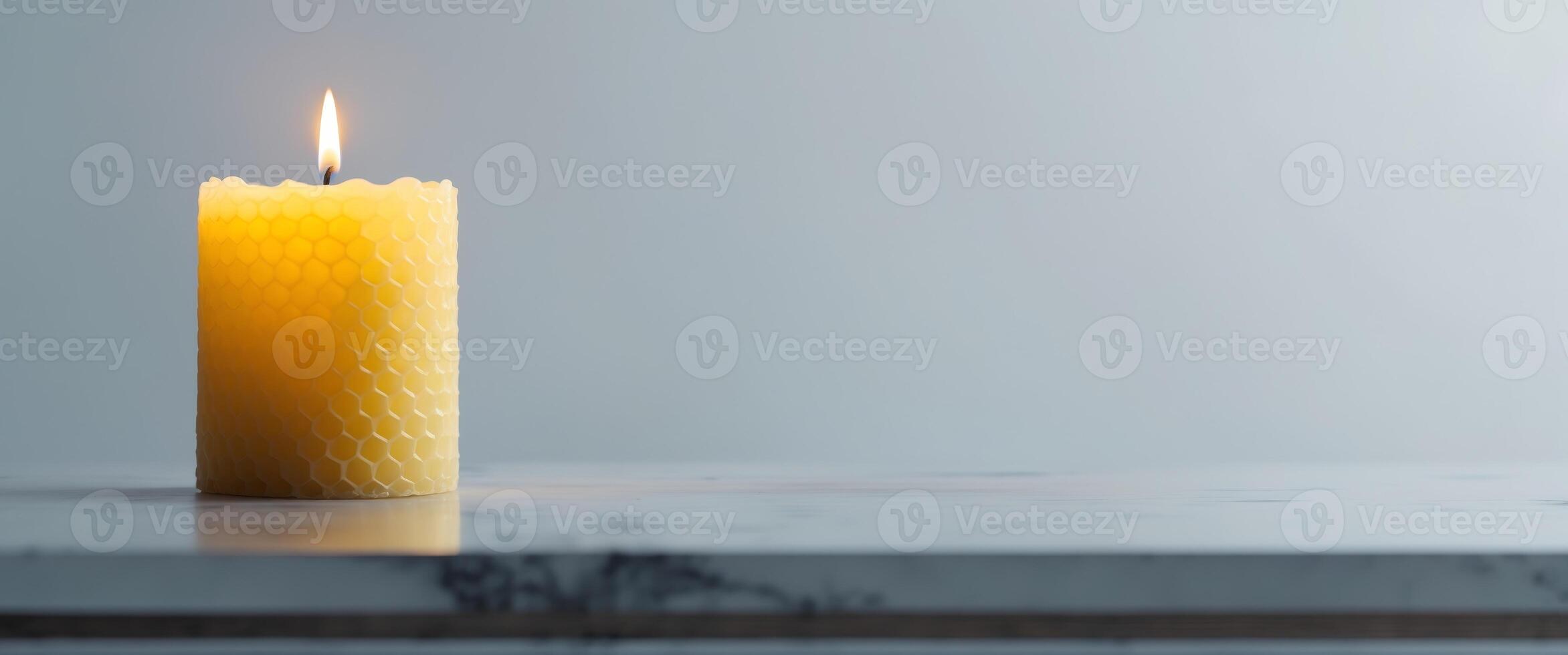 A single lit yellow beeswax candle sits on a surface photo