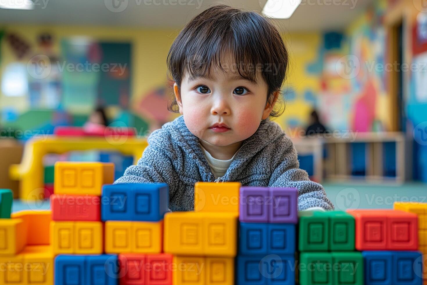 In cheerful playroom Asian child focuses on stacking colorful blocks while bright murals create lively atmosphere. Warm indoor lighting adds comfort scene photo