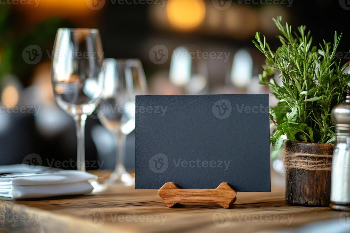 Empty chalkboard menu sign on restaurant table with wine glasses and herbs photo
