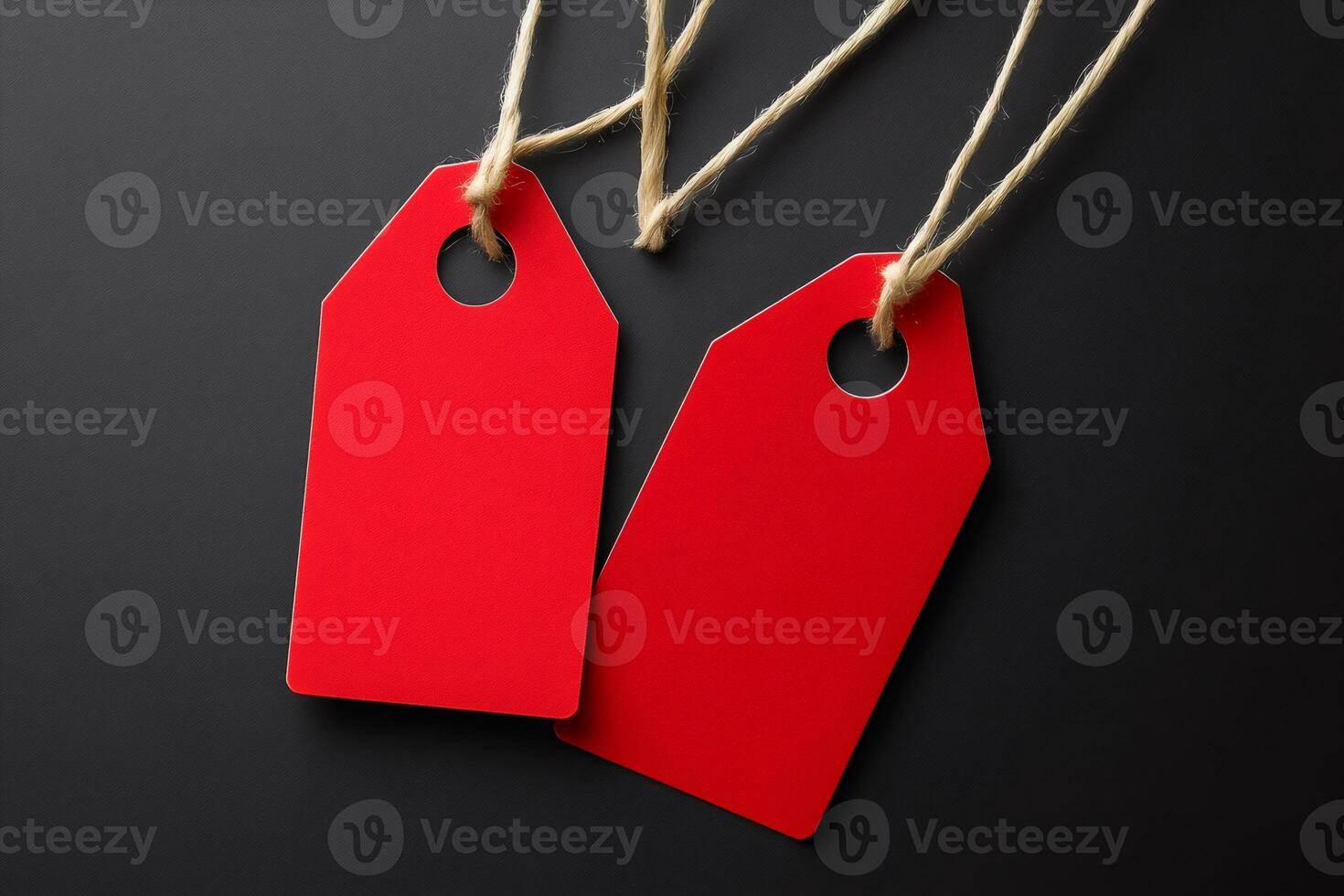 Two red blank price tags hanging on string against black background photo