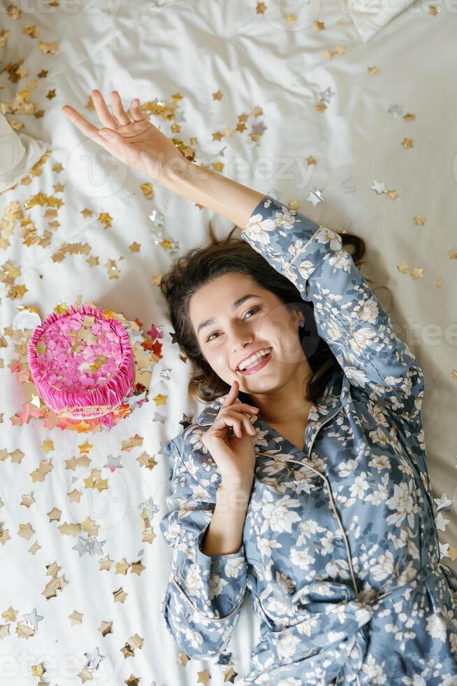 Young Woman Lying on Bed with Birthday Cake and Confetti, Enjoying the Celebration. photo