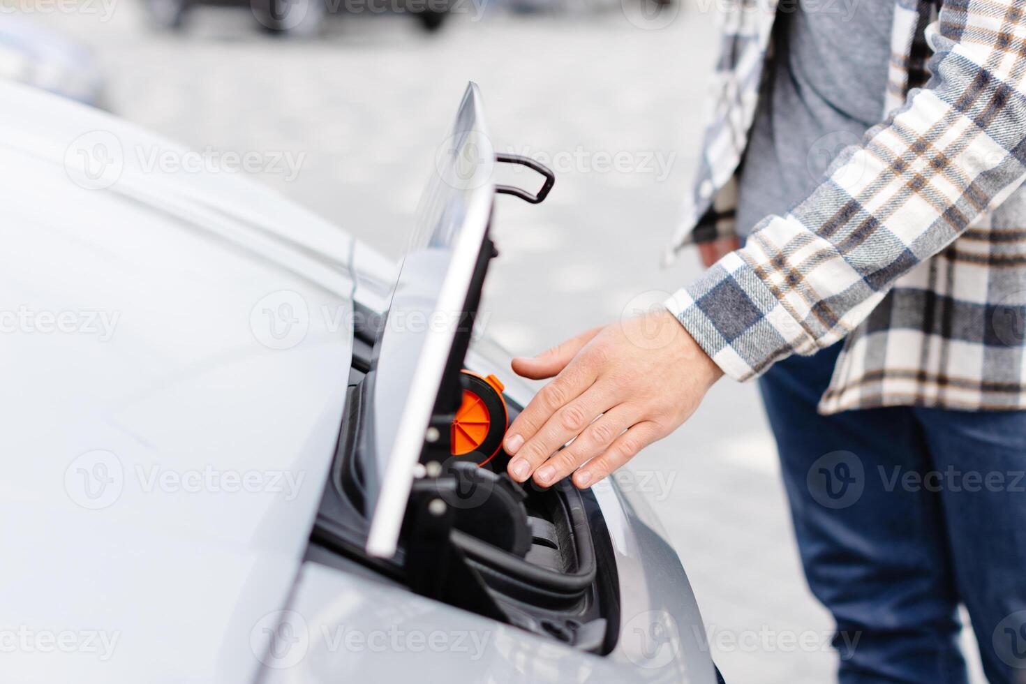 Young man plugging charging cable into the car socket. Electric car charging concept. photo