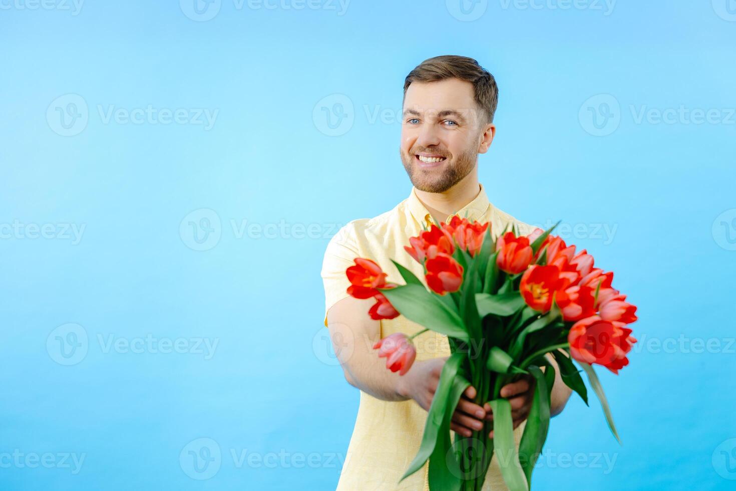 Man holding bouquet of red tulips on blue background photo