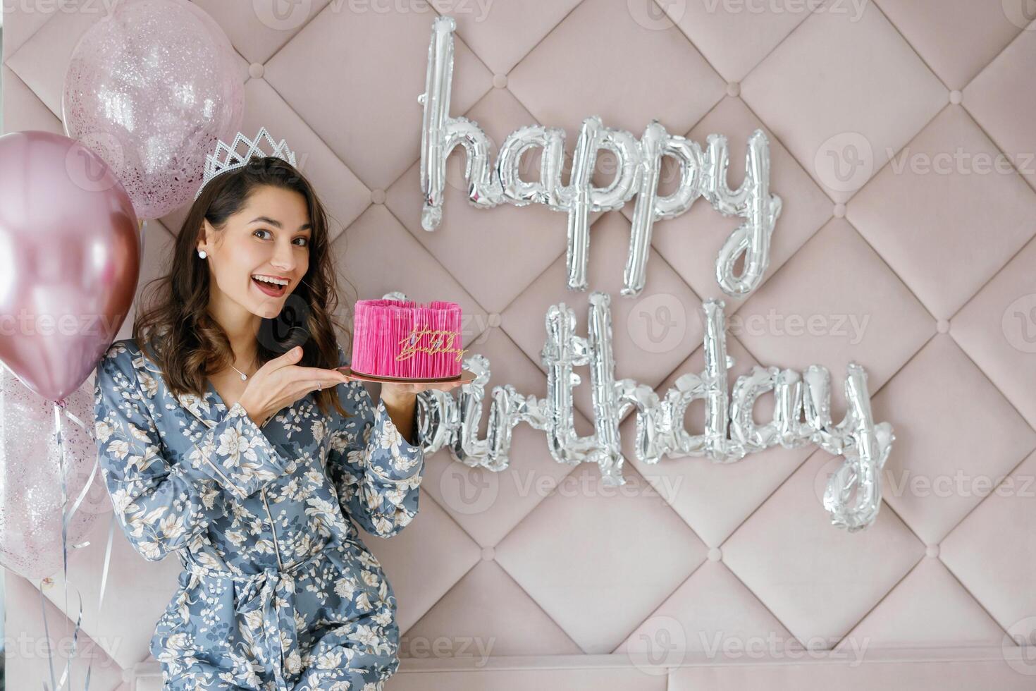 Woman celebrating birthday holding pink cake with balloons and happy birthday sign. photo