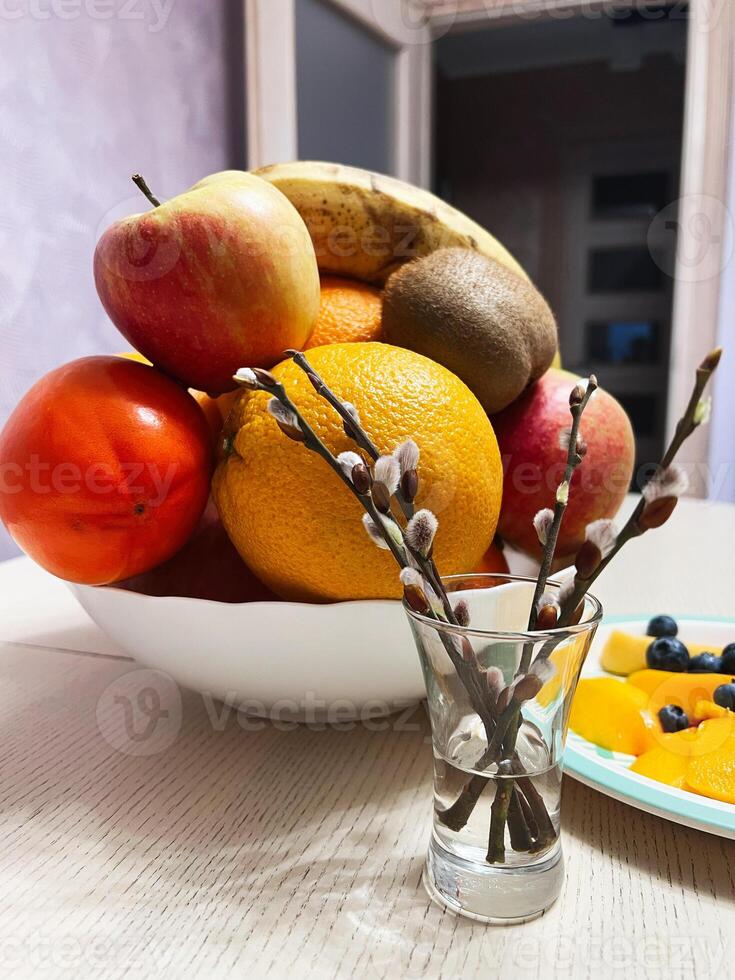 Fruit bowl and willow branches arranged on a wooden dining table photo