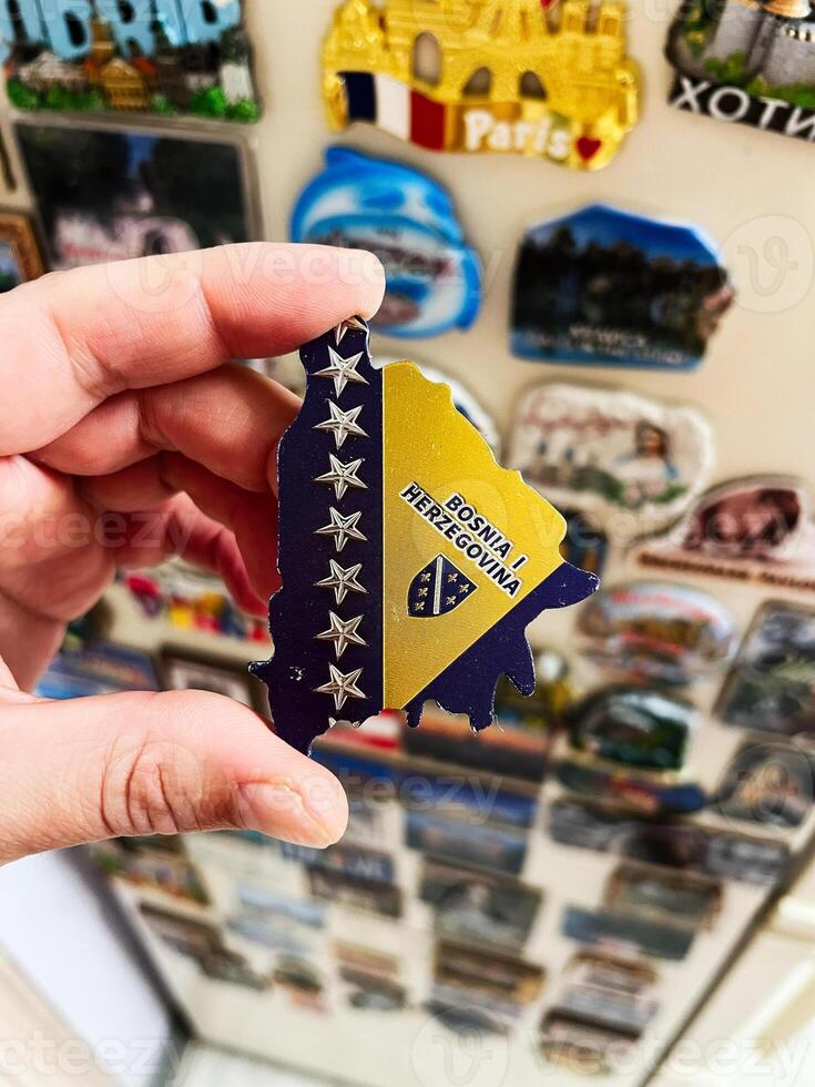 Hand holding Bosnia and Herzegovina magnet against colorful magnet collection photo