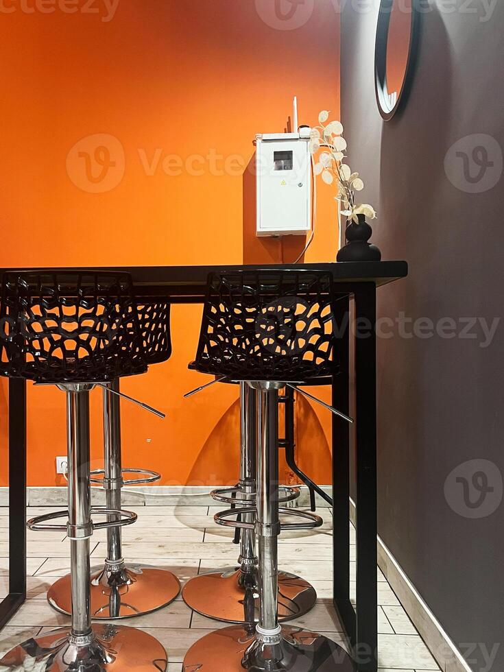 Modern seating area with orange wall and artistic metal bar stools photo