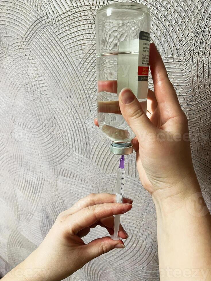 Hands drawing liquid medicine into a syringe with a sterile transparent vial photo