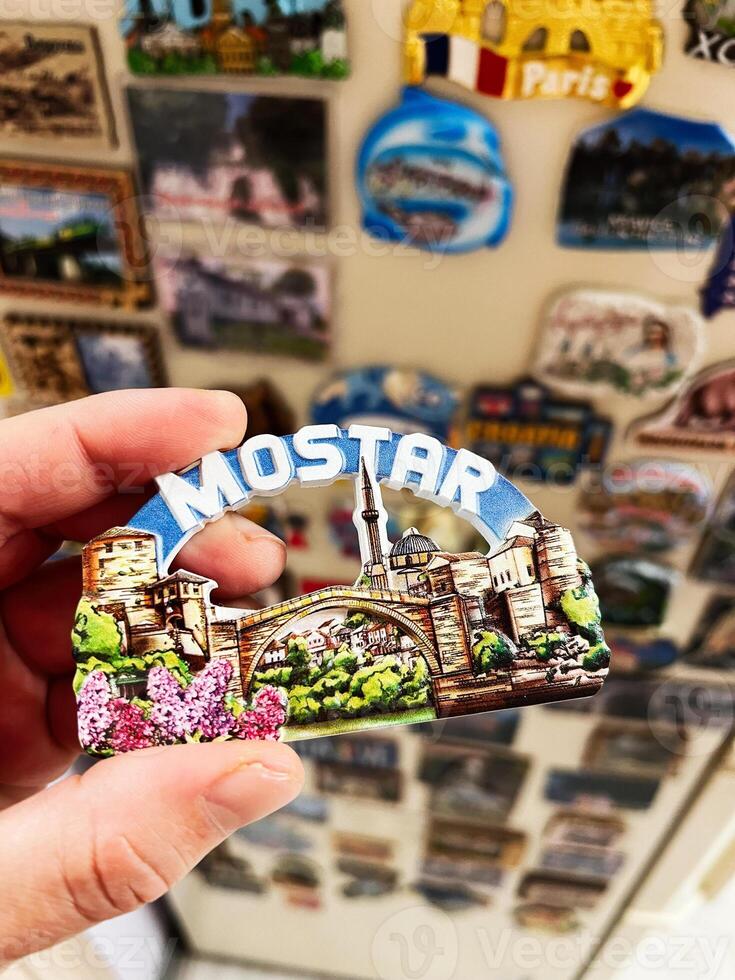 Hand holding a decorative souvenir featuring Mostar bridge design on fridge photo