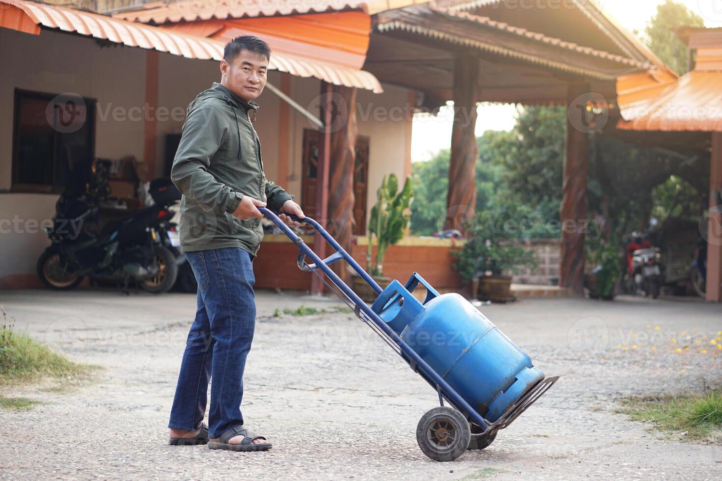 Asian man is pushing small cart that load blue gas cylinder tank to make delivery to local customer in rural of Thailand. Concept, Energy saving. Gas for cooking in daily life. Gas tank use with stove photo
