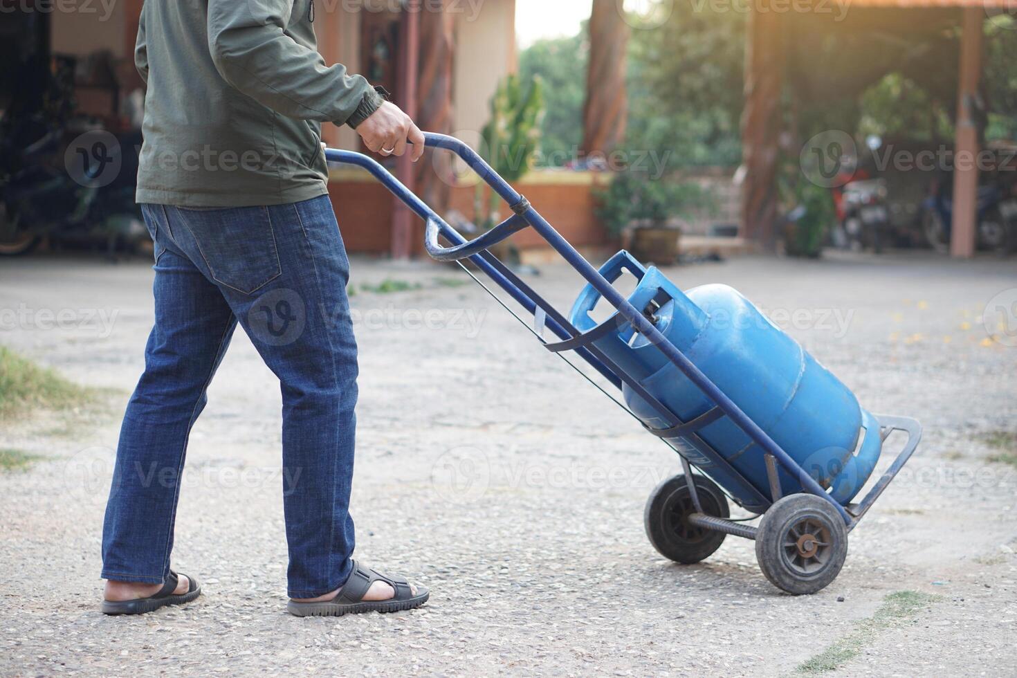 Close up man carries small cart that load blue gas cylinder tank to make delivery to local customer in rural of Thailand. Concept Energy saving Gas for cooking in daily life. Gas tank use with stove photo