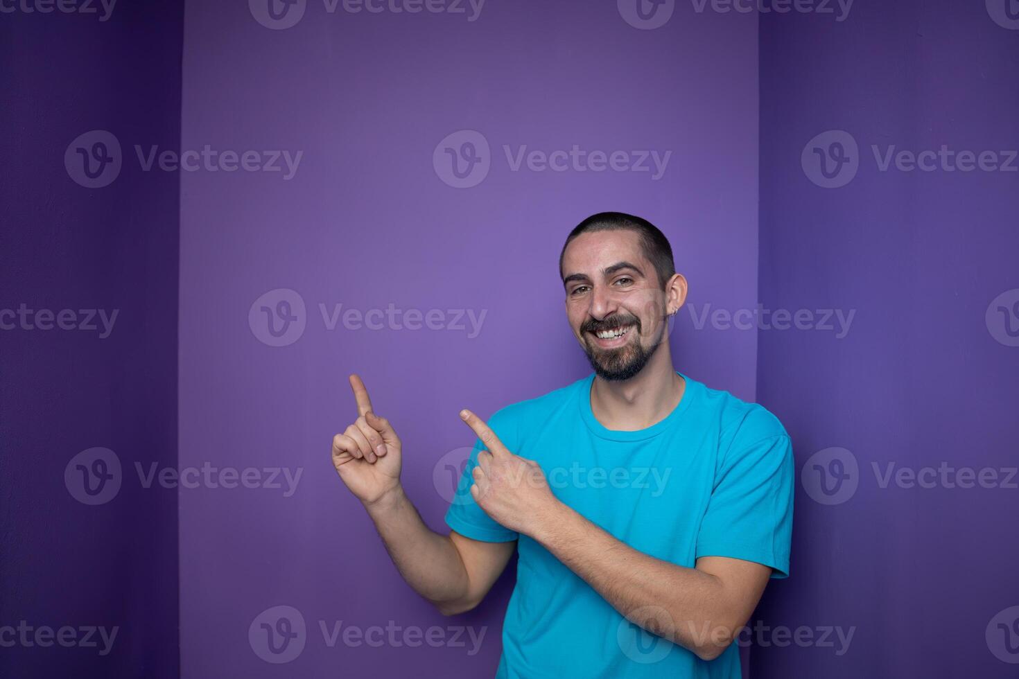 Smiling adult man introduce product, pointing finger against violet background with copy space. photo