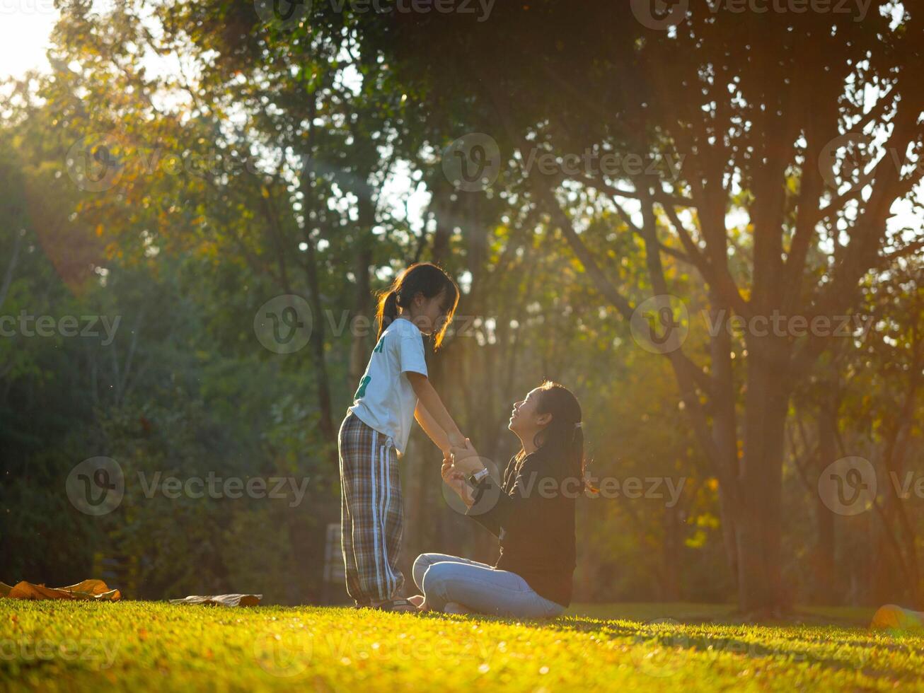 Mother and daughter are playing together in the park. Happy mother hugging her daughter sitting in the park with the sunset light. photo