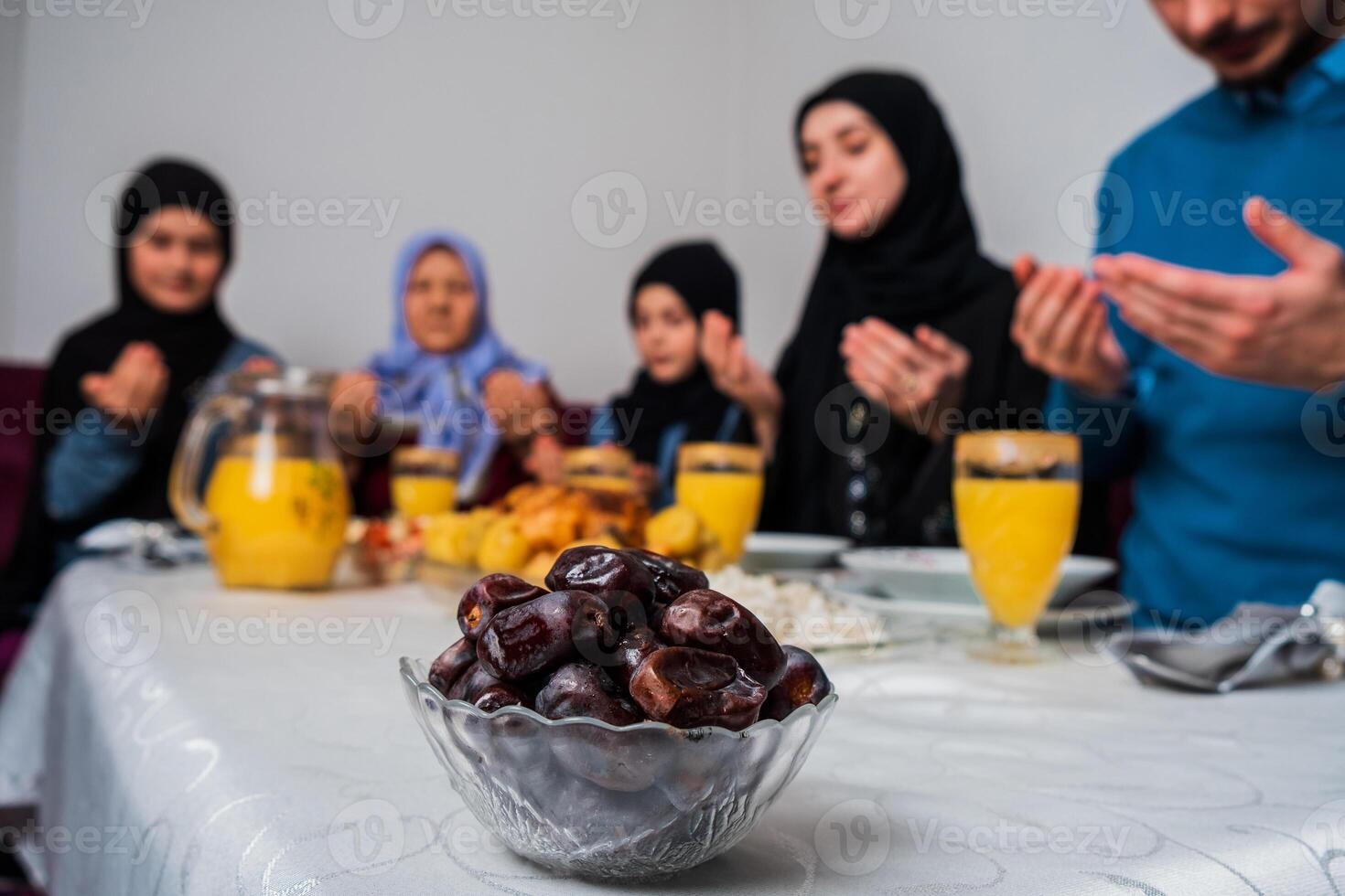 Happy Muslim family together making iftar dua to break fasting during Ramadan at the dining table at home focus on a bowl of dates healthy nutrition during the fast. photo