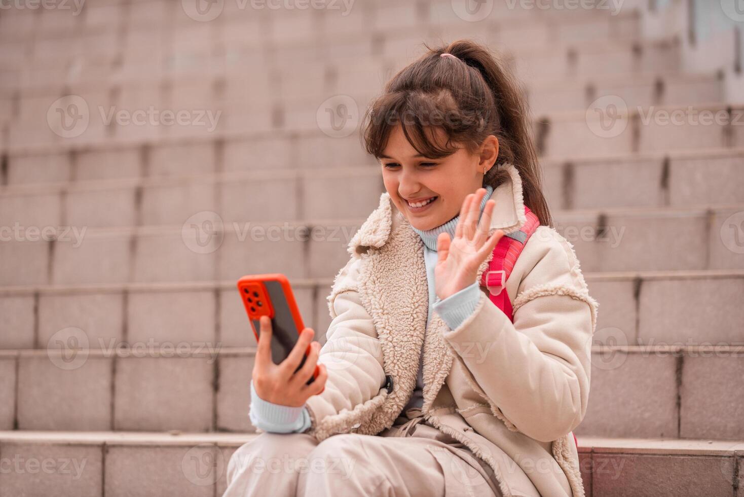A happy teenage girl taking call with mobile phone showing hi or bye outside in the city street. photo