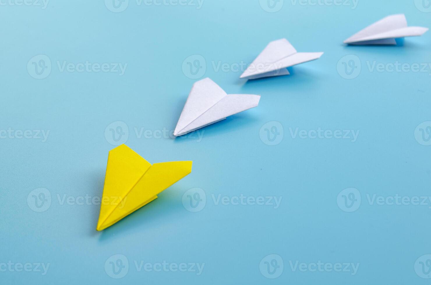 Origami paper airplane with yellow airplane leading the rest of white airplane photo