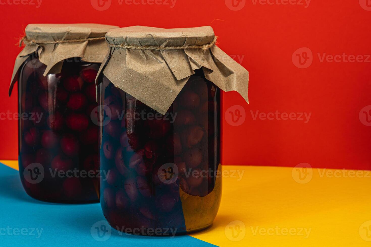Large jars of homemade cherry and raspberry jam on a colorful background photo