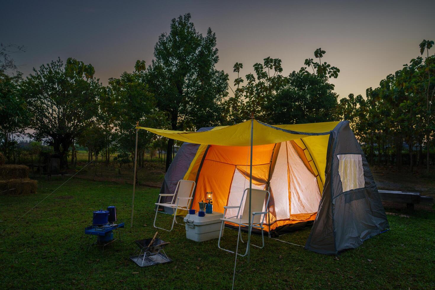 Camping tent on green grass at night, antique gas lamps, retro chairs, with outdoor coffee-making facilities on tables in a forest . photo