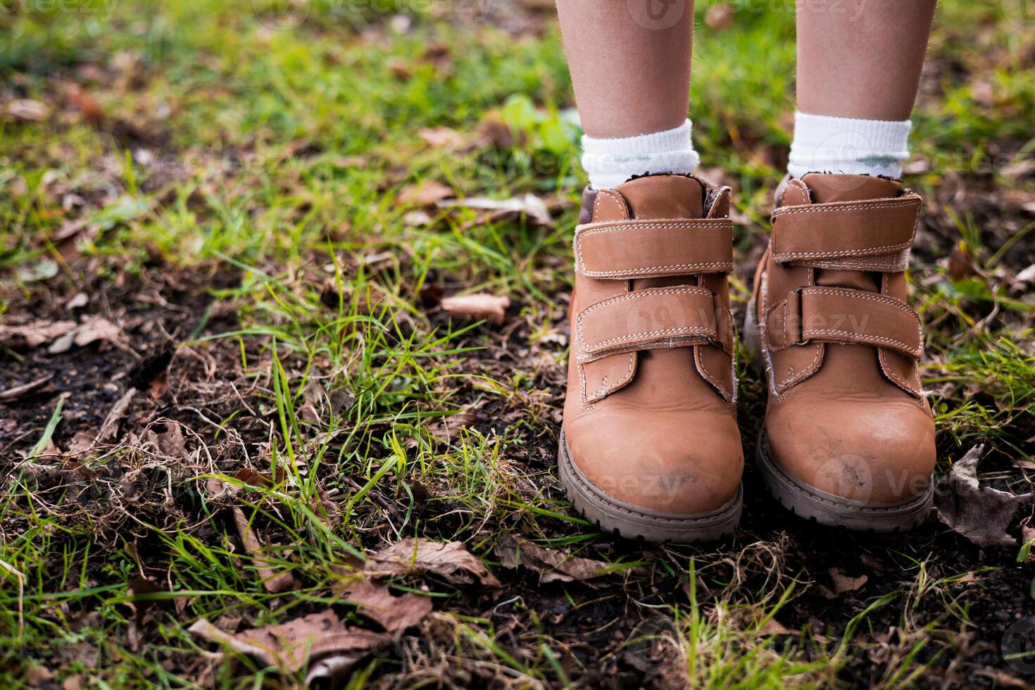 Childs brown boots on grass with autumn leaves photo