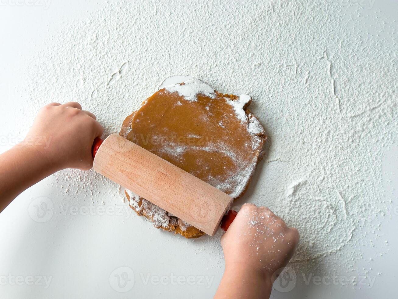 Child rolling dough on floured surface with rolling pin photo