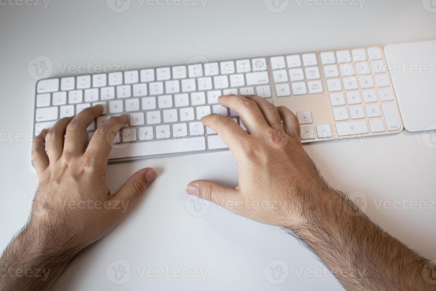 Male hands typing on wireless keyboard on white desk photo